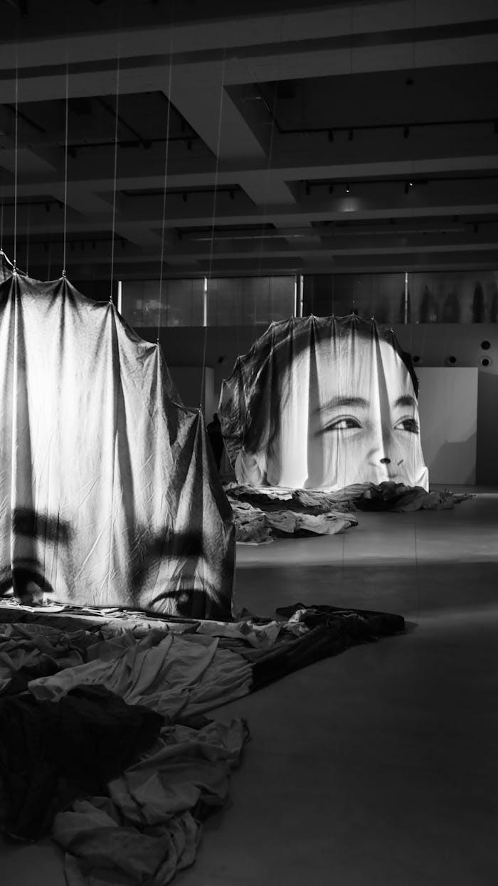 Black and white fabric art installation featuring human faces in an indoor gallery.